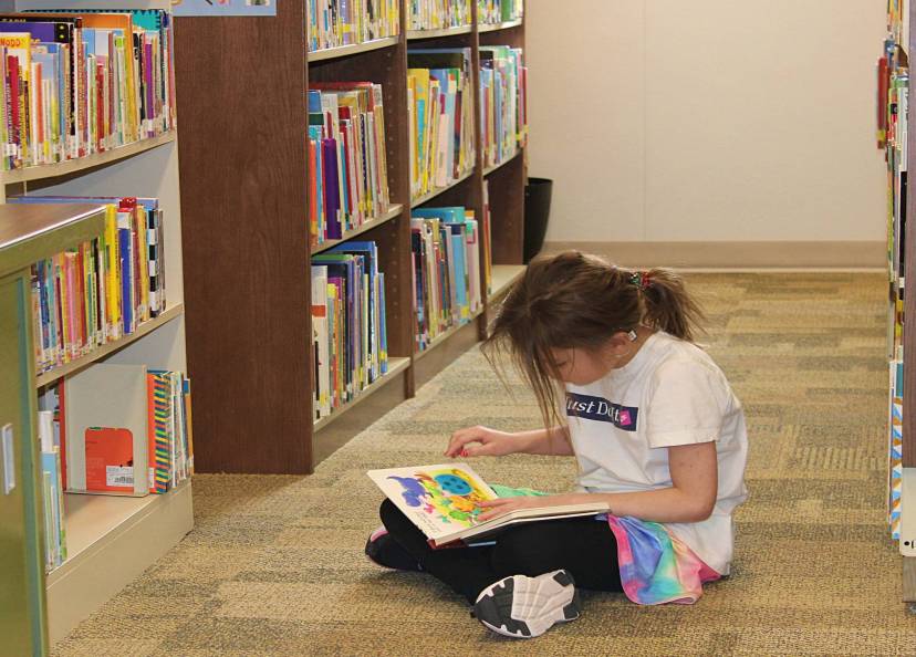 Student quietly sitting between book aisle reading